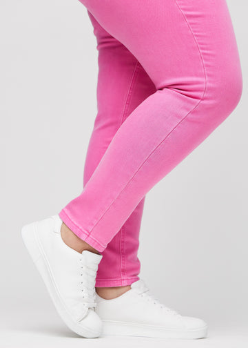 Slimjeans för kvinnor i ljusrosa, färgen Flamingos. Närbild vid anklarna på en plus size-modell som visar passformen vid bensluten.