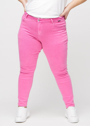 Slimjeans för kvinnor i ljusrosa, färgen Flamingos. Framifrån på en plus size-modell, med kroppsnära ben och lite mer utrymme vid anklarna.