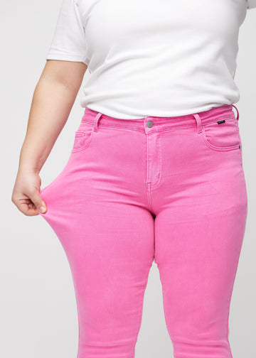 Slimjeans för kvinnor i ljusrosa, färgen Flamingos. En plus size-modell drar i jeanstyget vid låret för att visa stretchen.