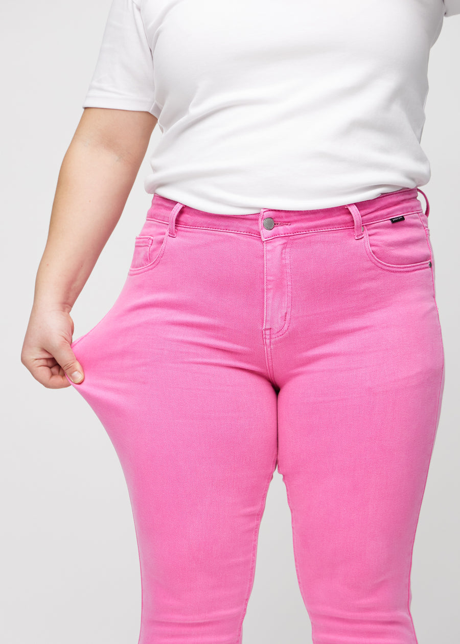 Slimjeans för kvinnor i ljusrosa, färgen Flamingos. En plus size-modell drar i jeanstyget vid låret för att visa stretchen.