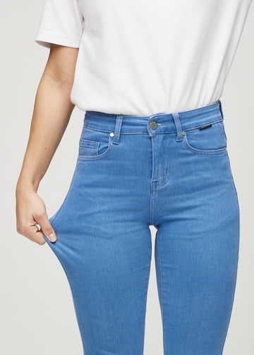 Slimjeans för kvinnor i blå, färgen Geraniums. En modell drar i jeanstyget vid låret för att visa stretchen.