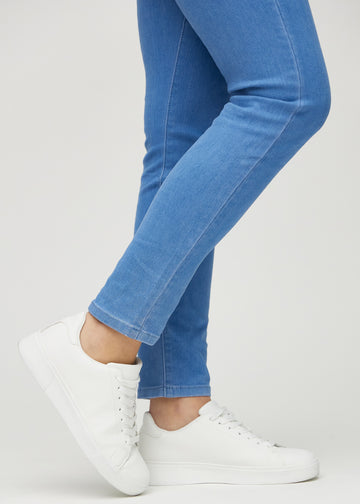 Slimjeans för kvinnor i blå, färgen Geraniums. Närbild vid anklarna på en modell som visar passformen vid bensluten.