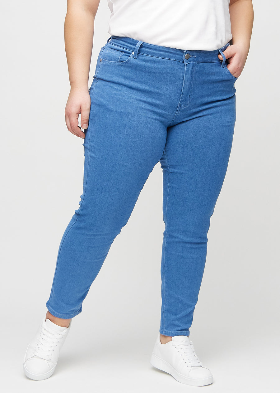 Slimjeans för kvinnor i blå, färgen Geraniums. Framifrån på en plus size-modell, med kroppsnära ben och lite mer utrymme vid anklarna.