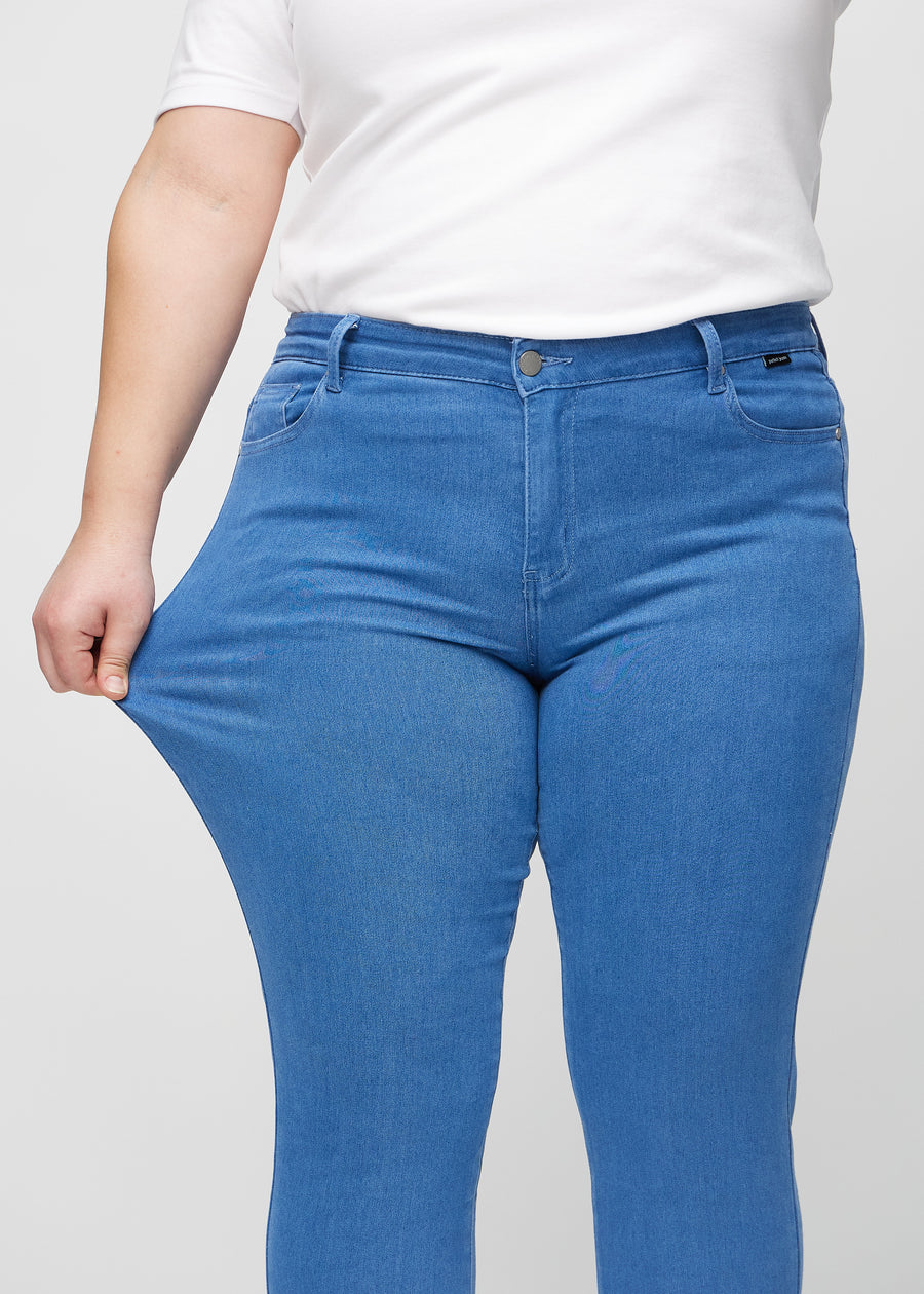 Slimjeans för kvinnor i blå, färgen Geraniums. En plus size-modell drar i jeanstyget vid låret för att visa stretchen.