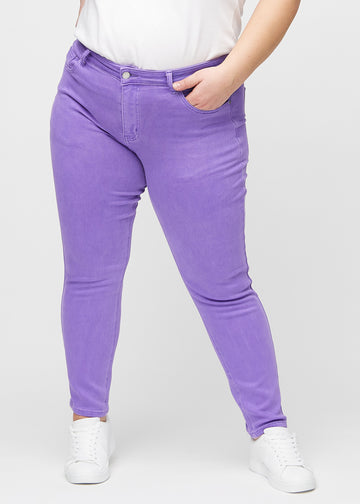 Slimjeans för kvinnor i lila, färgen Lavenders. Framifrån på en plus size-modell, med kroppsnära ben och lite mer utrymme vid anklarna.