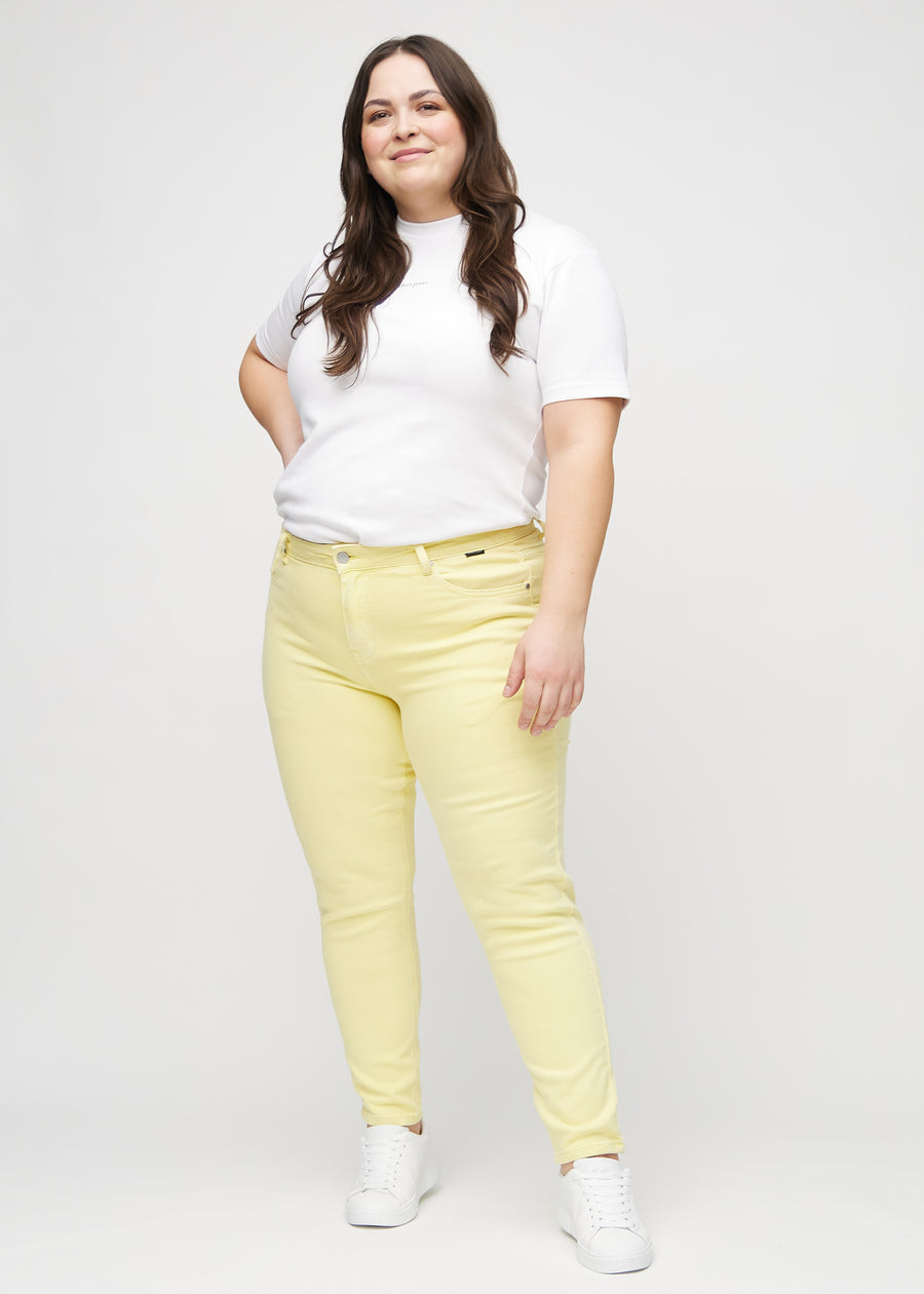 Slimjeans för kvinnor i ljusgul, färgen Lemonades. Helbild av en plus size-modell som bär jeansen.