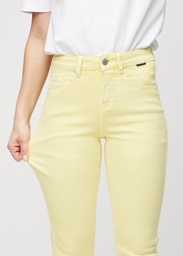 Slimjeans för kvinnor i ljusgul, färgen Lemonades. En modell drar i jeanstyget vid låret för att visa stretchen.