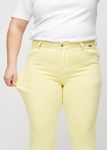 Slimjeans för kvinnor i ljusgul, färgen Lemonades. En plus size-modell drar i jeanstyget vid låret för att visa stretchen.