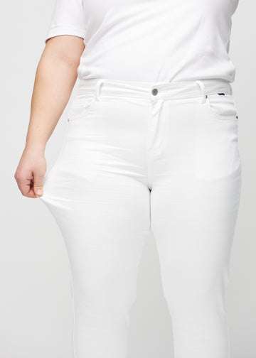 Slimjeans för kvinnor i vit, färgen Marguerites. En plus size-modell drar i jeanstyget vid låret för att visa stretchen.