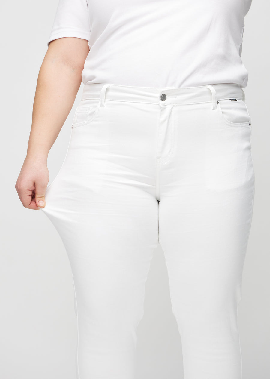 Slimjeans för kvinnor i vit, färgen Marguerites. En plus size-modell drar i jeanstyget vid låret för att visa stretchen.