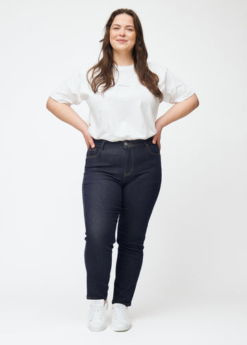 Helbild av plus-size-modell i djupt mörkblå denim jeans för kvinnor i färgen Midnights med slim passform.