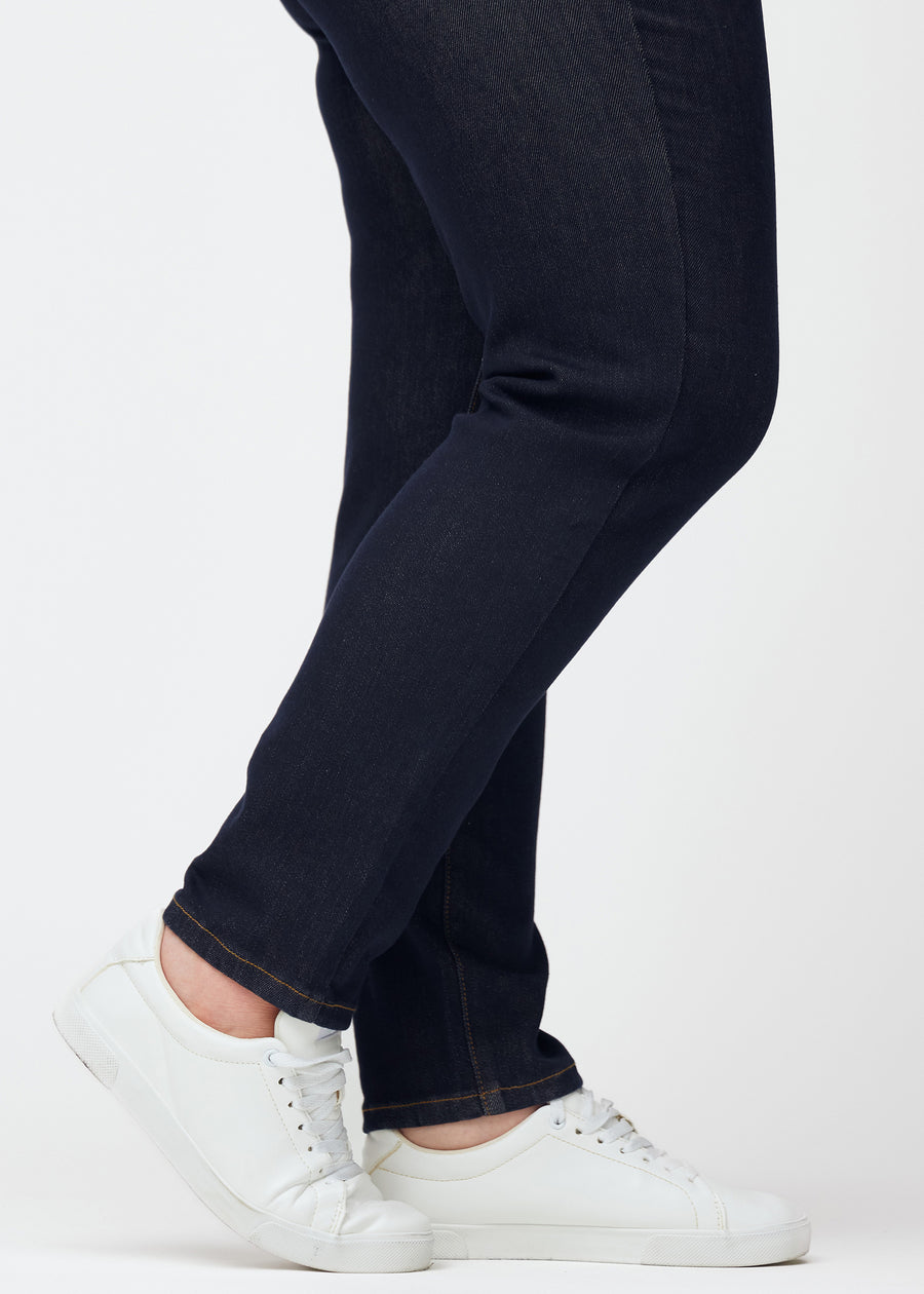 Djupt mörkblå denim jeans för kvinnor i färgen Midnights med slim passform sedd i närbild vid anklarna på plus-size-modell för att visa den figursydda avslutningen.