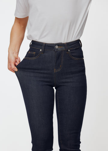 Modell stretchar den djupt mörkblå denimen jeans för kvinnor i färgen Midnights vid låret för att visa materialets stretch.