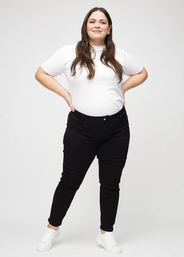 Slimjeans för kvinnor i svart, färgen Ravens. Helbild av en plus size-modell som bär jeansen.