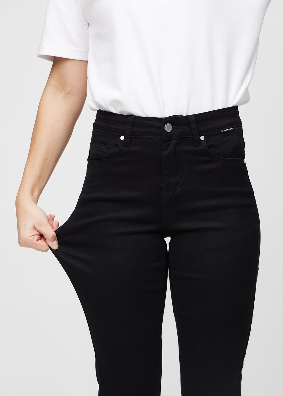 Slimjeans för kvinnor i svart, färgen Ravens. En modell drar i jeanstyget vid låret för att visa stretchen.