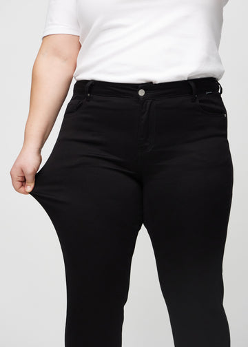 Slimjeans för kvinnor i svart, färgen Ravens. En plus size-modell drar i jeanstyget vid låret för att visa stretchen.