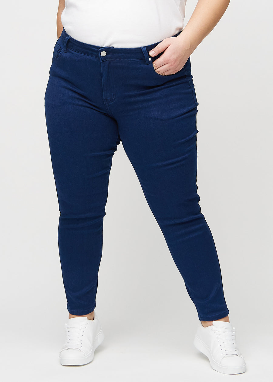 Slimjeans för kvinnor i mörkblå, färgen Royals. Framifrån på en plus size-modell, med kroppsnära ben och lite mer utrymme vid anklarna.