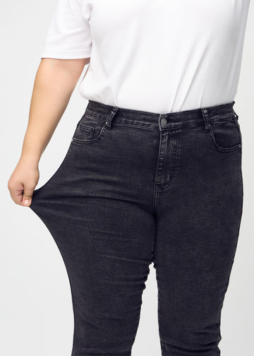 Slimjeans för kvinnor i mörkgrå, färgen Shadows. En plus size-modell drar i jeanstyget vid låret för att visa stretchen.