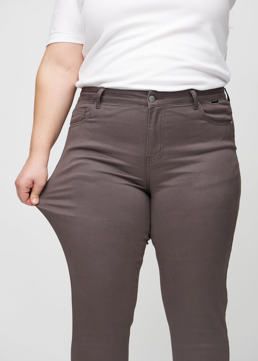 Slimjeans för kvinnor i gråbrun, färgen Thunders. En plus size-modell drar i jeanstyget vid låret för att visa stretchen.