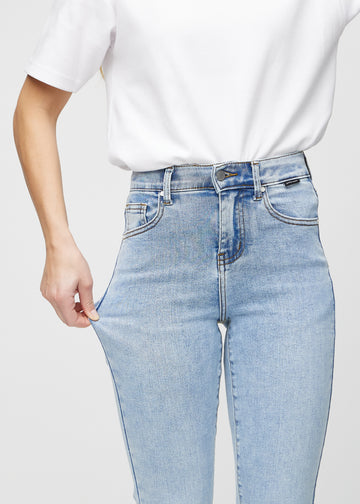 Slimjeans för kvinnor i ljusblå, färgen Waves. En modell drar i jeanstyget vid låret för att visa stretchen.