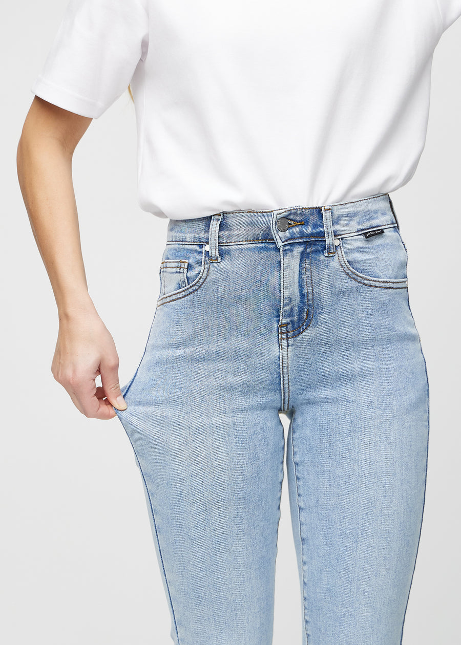 Slimjeans för kvinnor i ljusblå, färgen Waves. En modell drar i jeanstyget vid låret för att visa stretchen.