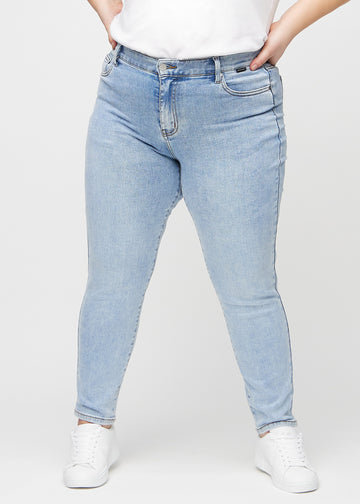 Slimjeans för kvinnor i ljusblå, färgen Waves. Framifrån på en plus size-modell, med kroppsnära ben och lite mer utrymme vid anklarna.