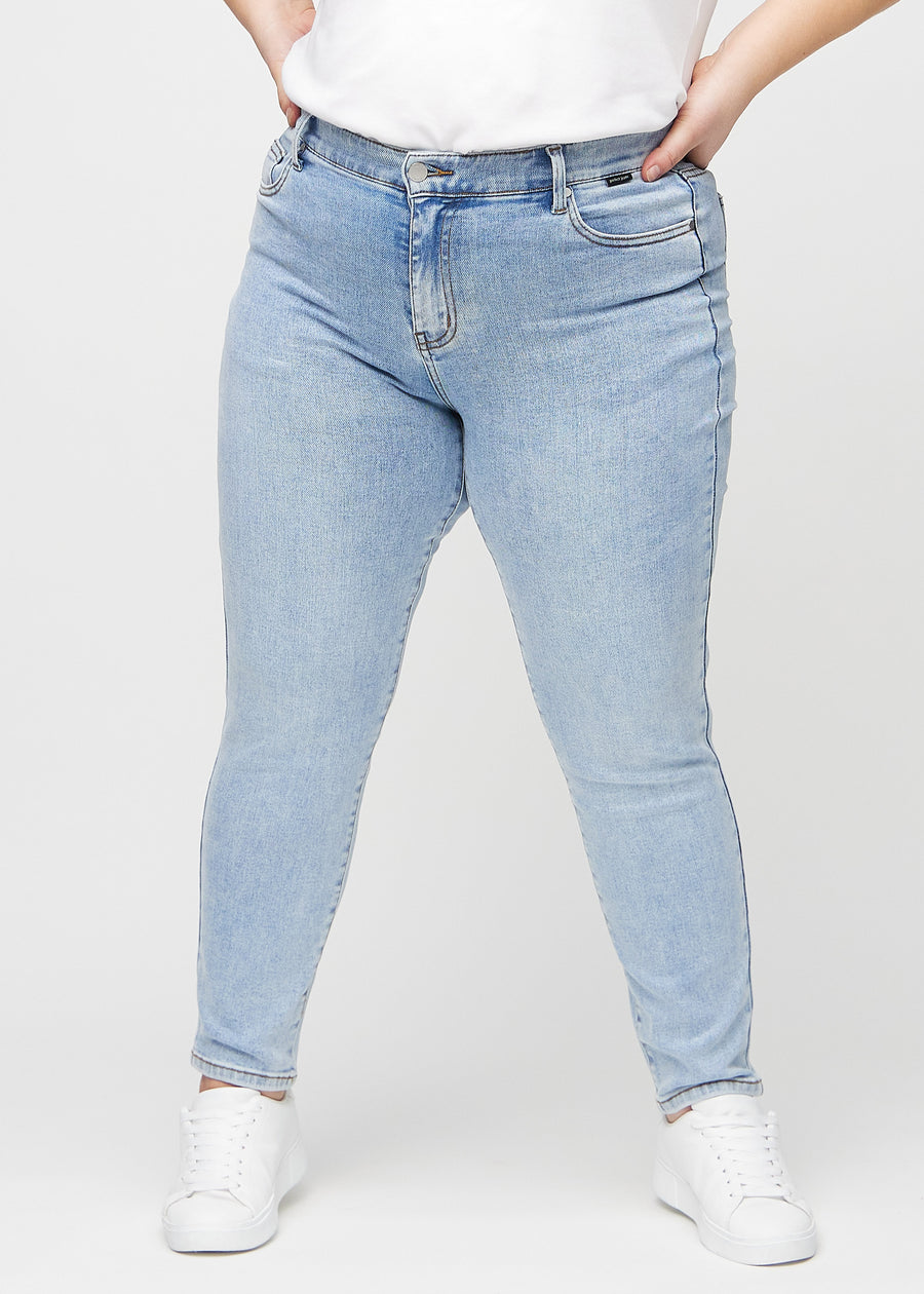 Slimjeans för kvinnor i ljusblå, färgen Waves. Framifrån på en plus size-modell, med kroppsnära ben och lite mer utrymme vid anklarna.