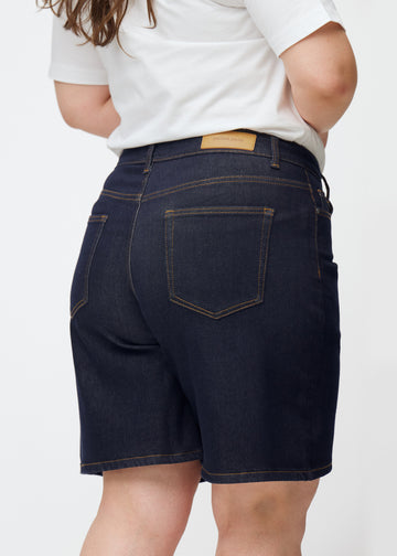 Mörkblå denimshorts för dam i färgen Midnights sett bakifrån i närbild på plus-size modell.