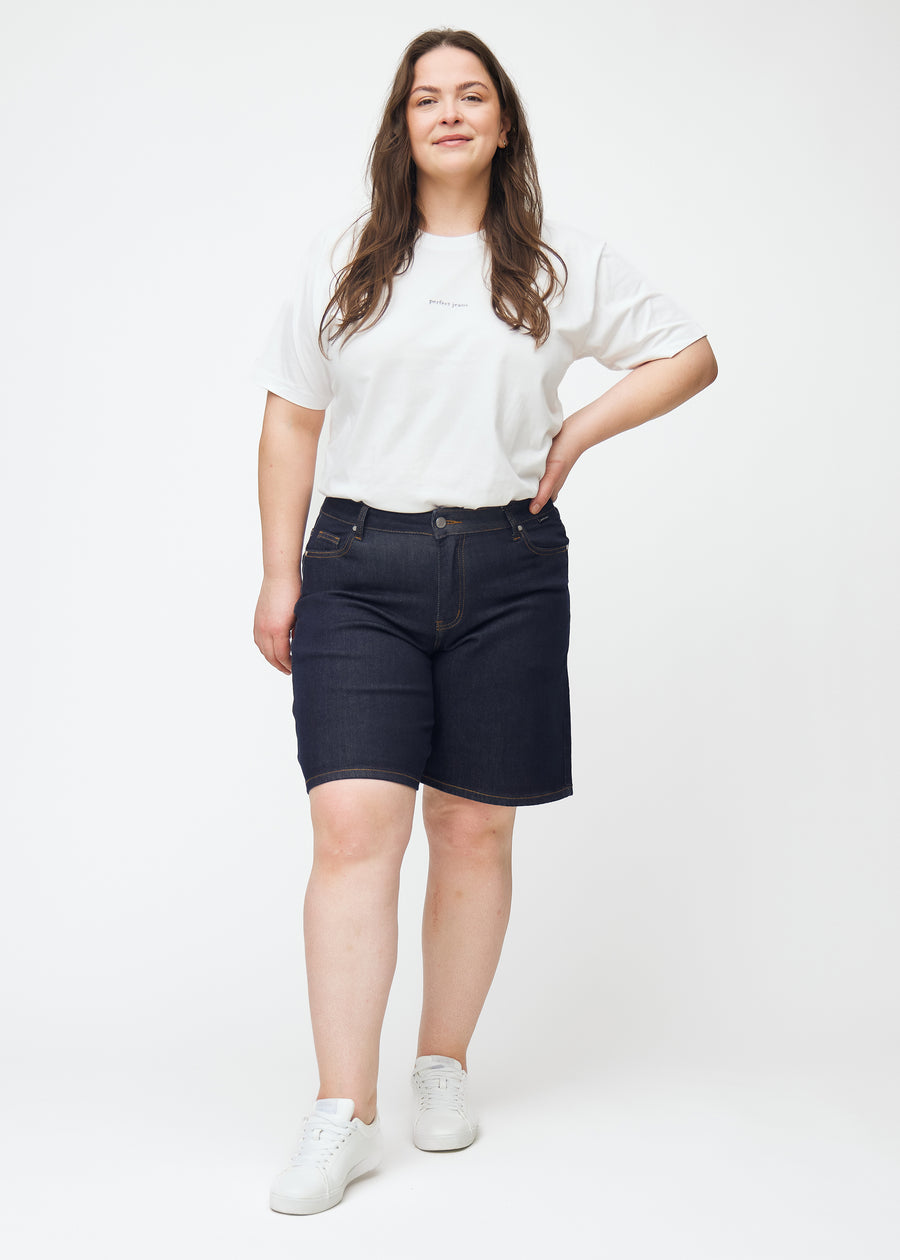Helbild av plus-size modell i mörkblå denimshorts för dam i färgen Midnights med loose passform.