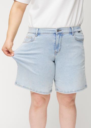 Kvinnlig modell drar i ljusblå Waves denimshorts vid låret för att visa materialets stretch.