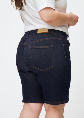 Mörkblå denimshorts för dam i färgen Midnights sett bakifrån i närbild på plus-size modell.