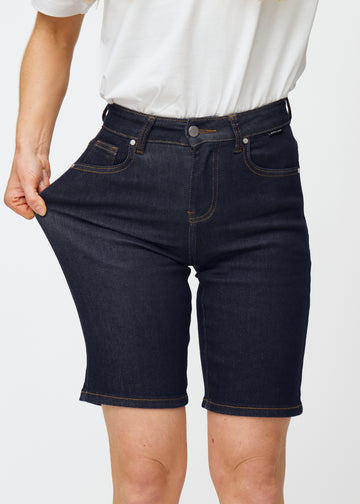 Modell sträcker mörkblå denimshorts för dam i färgen Midnights vid låret för att visa materialets stretch.