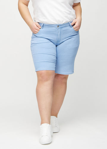 Ljusblå regular middle shorts, modellnamn Skies, som går rakt ner längs benet och slutar precis ovanför knät på en plus size-modell, sedd framifrån.