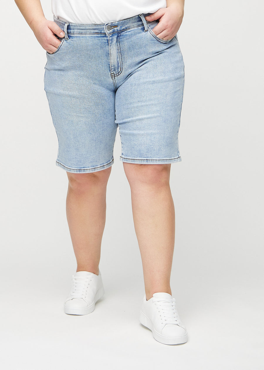 Ljus denim regular middle shorts, modellnamn Waves, som går rakt ned längs benet och slutar precis ovanför knät på en plus-size-modell, sedd framifrån.