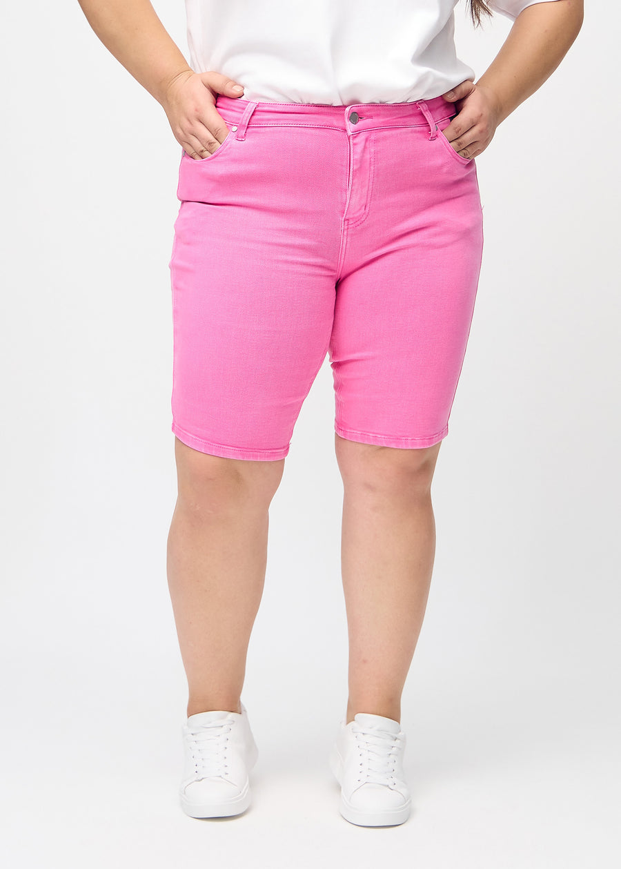 Ljusrosa skinny middle shorts, modellnamn Flamingos, som sitter tätt över låret och slutar precis ovanför knät på en plus size-modell, sedd framifrån.