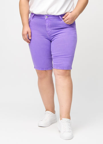Lila skinny middle shorts, modellnamn Lavenders, som sitter tätt över låret och slutar precis ovanför knät på en plus size-modell, framifrån.