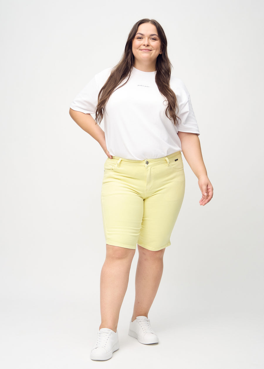 Helbild av en plus size-modell i ljusgula skinny middle shorts.