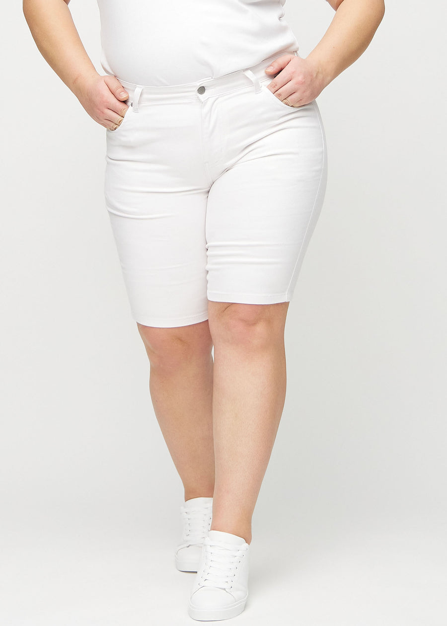Vita skinny middle shorts, modellnamn Marguerites, som sitter tight över låret och slutar precis ovanför knät på en plus-size-modell, sedda framifrån.