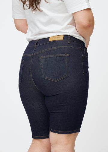 Mörkblå denimshorts för dam i färgen Midnights sett bakifrån i närbild på plus-size modell.