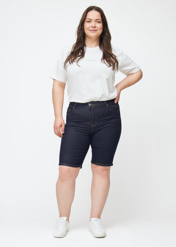 Helbild av plus-size modell i mörkblå denimshorts för dam i färgen Midnights med skinny passform.