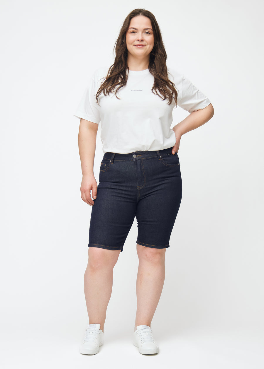 Helbild av plus-size modell i mörkblå denimshorts för dam i färgen Midnights med skinny passform.