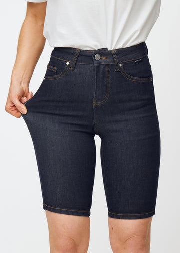 Modell sträcker mörkblå denimshorts för dam i färgen Midnights vid låret för att visa materialets stretch.