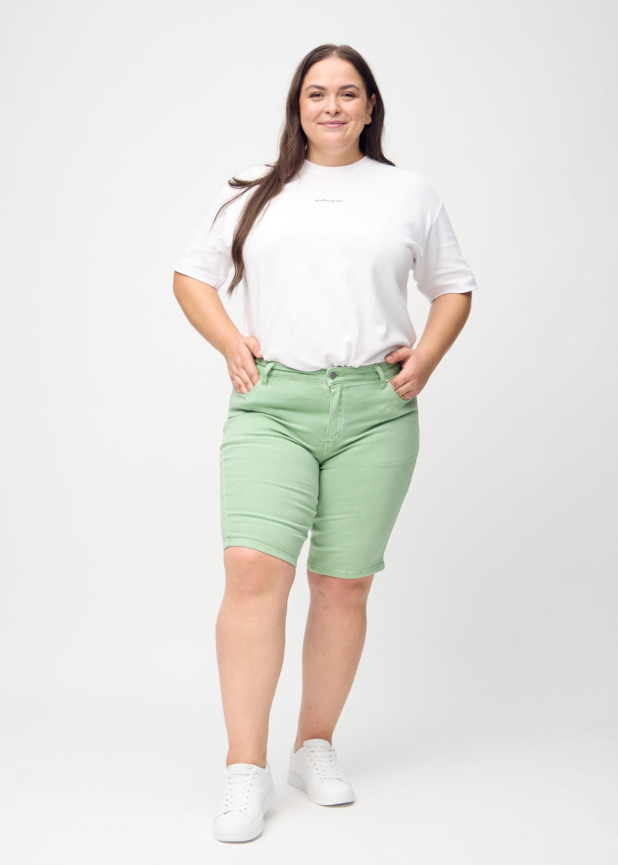 Helbild av en plus-size-modell i ljusgröna skinny middle shorts.