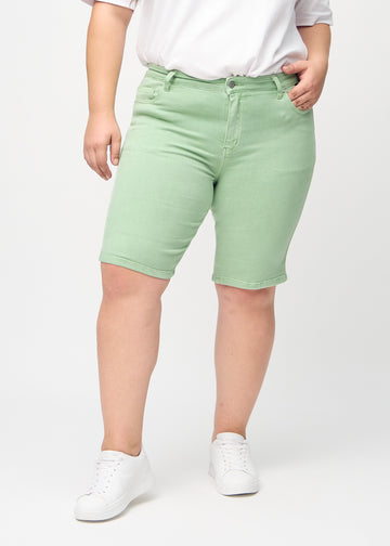 Ljusgröna skinny middle shorts, modellnamn Mints, som sitter tätt vid låret och slutar precis ovanför knät på en plus-size-modell, sedda framifrån.