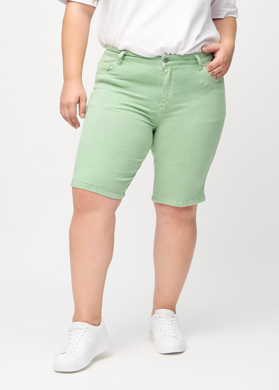 Ljusgröna skinny middle shorts, modellnamn Mints, som sitter tätt vid låret och slutar precis ovanför knät på en plus-size-modell, sedda framifrån.