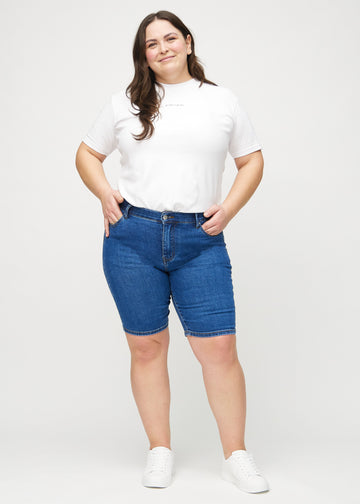 Helbild av en plus-size-modell i mörk denim skinny middle shorts.