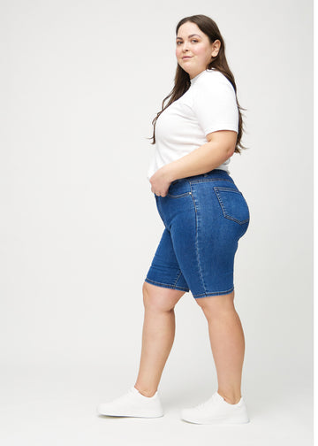 Mörk denim skinny middle shorts sedda från sidan på en plus-size-modell.