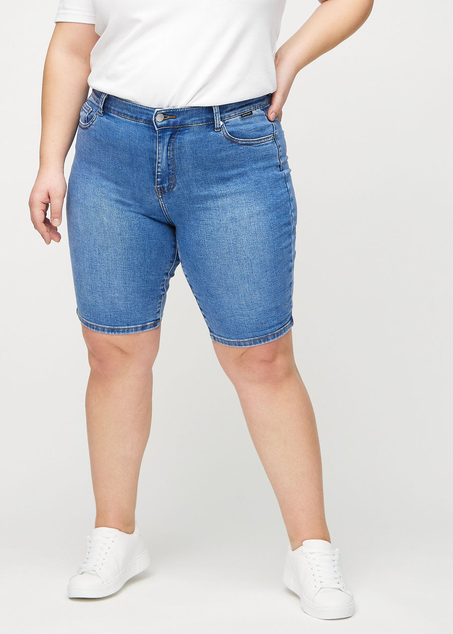 Denim skinny middle shorts, modellnamn Rivers, som sitter tight över låret och slutar precis ovanför knät på en plus size-modell, framifrån.