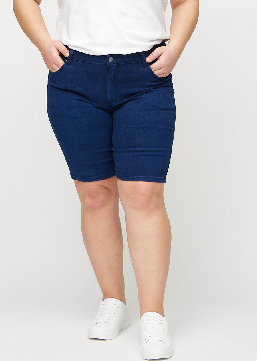 Mörkblå skinny middle shorts, modellnamn Royals, som sitter tätt mot låret och slutar precis ovanför knät på en plus-size-modell, sedd framifrån.