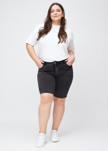 Helbild av en plus size-modell i mörkgrå denim skinny middle shorts.